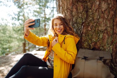 Seyahat ederken selfie. Elinde telefon olan mutlu bir kadın ormanda selfie çekiyor. Yaşam tarzı, seyahat, turizm, aktif yaşam.