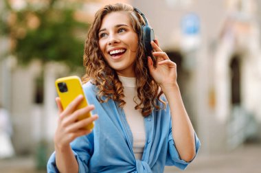 Genç bir kadın güzel müzik dinlemek ve şehirde yürümek için kulaklık kullanıyor. Kadın aşkı onu rahatlatan ve hayattan zevk alan müziği dinler. Seyahat, turizm, teknoloji, blog konsepti.