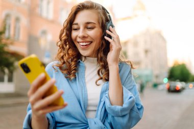 Genç bir kadın güzel müzik dinlemek ve şehirde yürümek için kulaklık kullanıyor. Kadın aşkı onu rahatlatan ve hayattan zevk alan müziği dinler. Seyahat, turizm, teknoloji, blog konsepti.