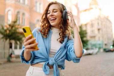 Genç bir kadın güzel müzik dinlemek ve şehirde yürümek için kulaklık kullanıyor. Kadın aşkı onu rahatlatan ve hayattan zevk alan müziği dinler. Seyahat, turizm, teknoloji, blog konsepti.