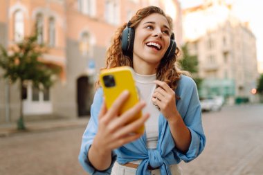Genç bir kadın güzel müzik dinlemek ve şehirde yürümek için kulaklık kullanıyor. Kadın aşkı onu rahatlatan ve hayattan zevk alan müziği dinler. Seyahat, turizm, teknoloji, blog konsepti.