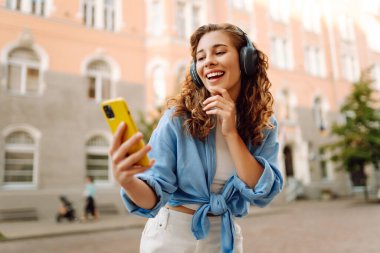 Genç bir kadın güzel müzik dinlemek ve şehirde yürümek için kulaklık kullanıyor. Kadın aşkı onu rahatlatan ve hayattan zevk alan müziği dinler. Seyahat, turizm, teknoloji, blog konsepti.