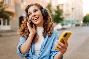 Genç bir kadın güzel müzik dinlemek ve şehirde yürümek için kulaklık kullanıyor. Kadın aşkı onu rahatlatan ve hayattan zevk alan müziği dinler. Seyahat, turizm, teknoloji, blog konsepti.