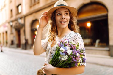 Elinde bir buket yabani çiçekle sokaklarda yürüyen mutlu genç bir kadın. Duygular. Moda tarzı