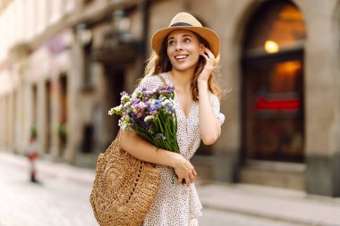 Elinde bir buket yabani çiçekle sokaklarda yürüyen mutlu genç bir kadın. Duygular. Moda tarzı