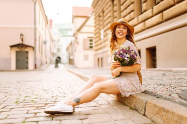 Elinde bir buket yabani çiçekle sokaklarda yürüyen mutlu genç bir kadın. Duygular. Moda tarzı