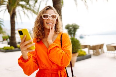 Şehir caddesinde akıllı cep telefonuyla yürüyen çekici genç kadın turist, internette gezinen, arama yapan. Teknoloji ve yaşam tarzı seyahat ve seyahat kavramı.