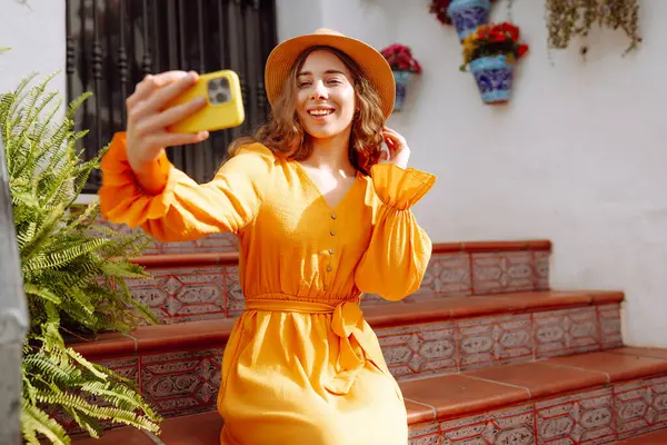 Sokakta selfie çekerken akıllı telefon kamerasına poz veren ve gülümseyen güzel bir genç kadın. Seyahat, blog, hafta sonu, rahatlama ve yaşam tarzı konsepti.