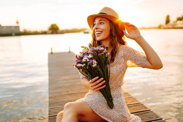Молодая женщина в платье сидит на деревянном пирсе возле пруда. Сельский стиль свадьбы. Путешествия, туризм, природа.