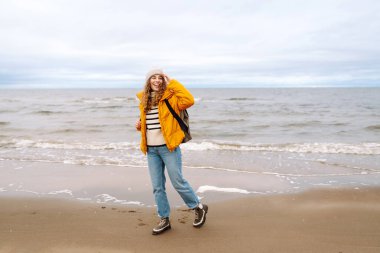 Bulutlu bir günde sahilde yürüyen genç bir kadın. Sahil şeridine giden şık bir kadın soğuk havada hayatı düşünüyor. Etkin yaşam biçimi.