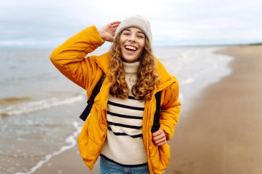 Bulutlu bir günde sahilde yürüyen genç bir kadın. Sahil şeridine giden şık bir kadın soğuk havada hayatı düşünüyor. Etkin yaşam biçimi.