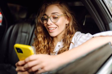 Emniyet kemeri takmış bir kadın içerideki telefonu kullanıyor. Teknoloji kavramı, araba ve iş seyahati..