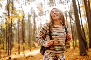 Sonbahar günü sırt çantasıyla ormanda yürüyüş yapan bir kadın yürüyüşçü. Doğa, seyahat, dinlenme konsepti.
