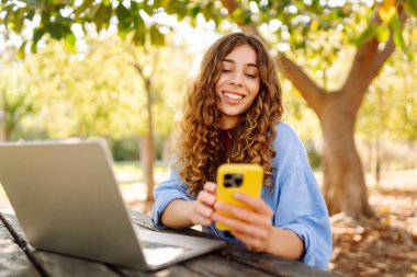 Dışarıda bankta otururken dizüstü bilgisayarda yazan genç bir kadın. Eğitim, iş, blog veya serbest çalışma kavramı.