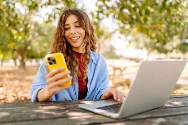 Dışarıda bankta otururken dizüstü bilgisayarda yazan genç bir kadın. Eğitim, iş, blog veya serbest çalışma kavramı.