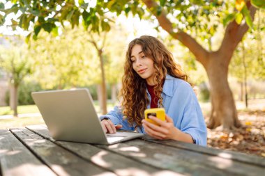 Dışarıda bankta otururken dizüstü bilgisayarda yazan genç bir kadın. Eğitim, iş, blog veya serbest çalışma kavramı.