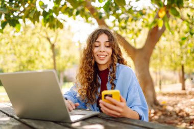 Dışarıda bankta otururken dizüstü bilgisayarda yazan genç bir kadın. Eğitim, iş, blog veya serbest çalışma kavramı.