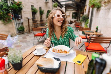Roma 'nın caddesindeki restoranda İtalyan makarnası yiyen genç bir kadın. İtalyan gastronomisi ve seyahat kavramı. Yiyecek ve içecek..