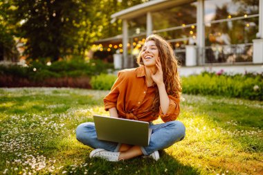 Genç bir kadın parkta oturmuş video görüşmesiyle iletişim kuruyor. Laptop bilgisayarına bakan bir kız, online konferans ofis sohbeti, sanal eğitim konsepti. Serbest Çalışan, Çevrimiçi Eğitim.