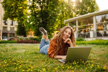 Genç bir kadın parkta oturmuş video görüşmesiyle iletişim kuruyor. Laptop bilgisayarına bakan bir kız, online konferans ofis sohbeti, sanal eğitim konsepti. Serbest Çalışan, Çevrimiçi Eğitim.