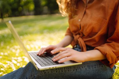 Genç bir kadın parkta oturmuş video görüşmesiyle iletişim kuruyor. Laptop bilgisayarına bakan bir kız, online konferans ofis sohbeti, sanal eğitim konsepti. Serbest Çalışan, Çevrimiçi Eğitim.