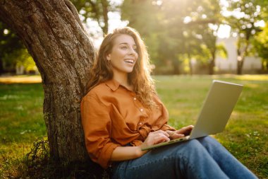 Genç bir kadın parkta oturmuş video görüşmesiyle iletişim kuruyor. Laptop bilgisayarına bakan bir kız, online konferans ofis sohbeti, sanal eğitim konsepti. Serbest Çalışan, Çevrimiçi Eğitim.