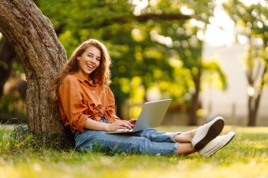 Genç bir kadın parkta oturmuş video görüşmesiyle iletişim kuruyor. Laptop bilgisayarına bakan bir kız, online konferans ofis sohbeti, sanal eğitim konsepti. Serbest Çalışan, Çevrimiçi Eğitim.