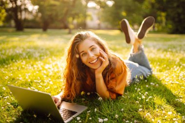 Genç bir kadın parkta oturmuş video görüşmesiyle iletişim kuruyor. Laptop bilgisayarına bakan bir kız, online konferans ofis sohbeti, sanal eğitim konsepti. Serbest Çalışan, Çevrimiçi Eğitim.