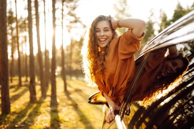 Genç bir kadın araba kullanırken pencereden dışarı bakarak taze rüzgarın tadını çıkarıyor. Yaşam tarzı, seyahat, turizm, doğa, aktif yaşam. Araba yolculuğu.