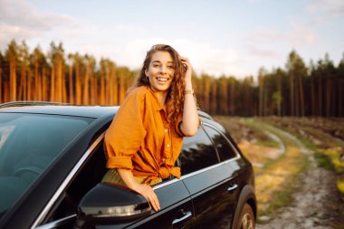 Genç bir kadın araba kullanırken pencereden dışarı bakarak taze rüzgarın tadını çıkarıyor. Yaşam tarzı, seyahat, turizm, doğa, aktif yaşam. Araba yolculuğu.