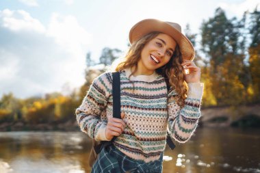 Sırt çantalı mutlu kadın gezgin nehir boyunca sonbahar yürüyüşünün tadını çıkarıyor. Aktif yaşam tarzı. Yürüyüş, seyahat, tatil konsepti.