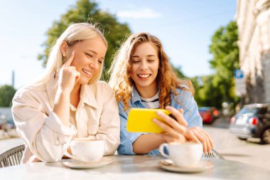 Yazlık kafede otururken mutlu kadınlar kahve içip cep telefonu kullanıyor. Moda, güzellik, blog, turizm.