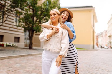 Şehir caddesinde yürüyen iki kadın yaz tatilinin tadını çıkarırken birlikte gülen mutlu genç kadınlar. Yaşam tarzı, moda, seyahat kavramı.
