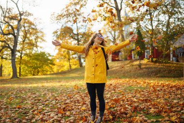 Elleri havada gülümseyen genç bir kadın ormandaki sonbahar yapraklarını fırlatıyor. Güzel bir yer. Rahatlama, eğlence, doğa ile yalnızlık kavramı..