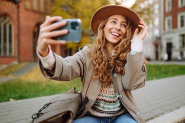 Kadın blogcu, sonbahar parkında blog yazıyor. Blogcu kadın video kayıtlarını ve kısa videolarını akıllı telefon kamerasıyla çekiyor. Seyahat blogu. Macera, tatil