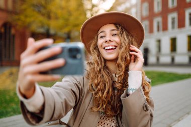 Kadın blogcu, sonbahar parkında blog yazıyor. Blogcu kadın video kayıtlarını ve kısa videolarını akıllı telefon kamerasıyla çekiyor. Seyahat blogu. Macera, tatil