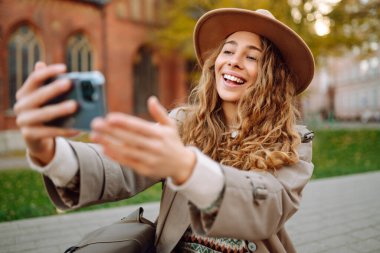 Kadın blogcu, sonbahar parkında blog yazıyor. Blogcu kadın video kayıtlarını ve kısa videolarını akıllı telefon kamerasıyla çekiyor. Seyahat blogu. Macera, tatil