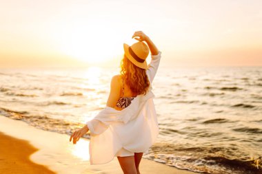 Sahilde yalınayak yürüyen genç bir kadın, gün doğumunda. Seyahat, hafta sonu, rahatlama ve yaşam tarzı konsepti.