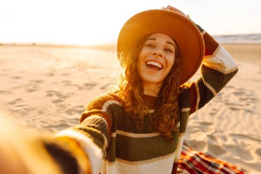 Genç bir kadın, güneş doğarken deniz dibinde cep telefonuyla selfie çekiyor. Soğuk hava. İnsanlar, tatil, yaşam tarzı, yolculuk konsepti.
