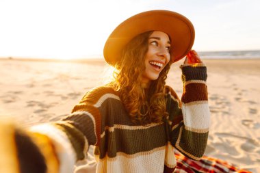 Genç bir kadın, güneş doğarken deniz dibinde cep telefonuyla selfie çekiyor. Soğuk hava. İnsanlar, tatil, yaşam tarzı, yolculuk konsepti.