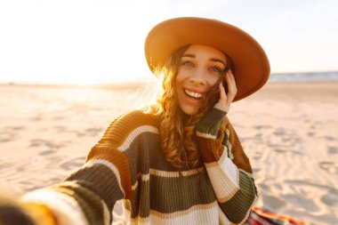 Genç bir kadın, güneş doğarken deniz dibinde cep telefonuyla selfie çekiyor. Soğuk hava. İnsanlar, tatil, yaşam tarzı, yolculuk konsepti.