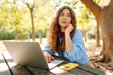 Dizüstü bilgisayarda yazı yazan kız öğrenci üniversite binası, eğitim ve modern teknolojilerin yanında oturuyor..
