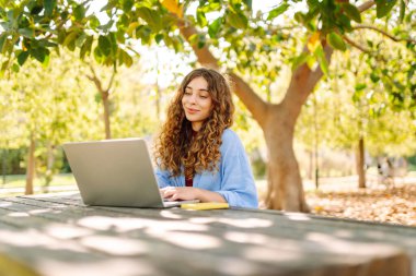 Dizüstü bilgisayarda yazı yazan kız öğrenci üniversite binası, eğitim ve modern teknolojilerin yanında oturuyor..