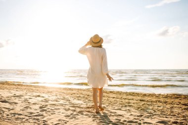Altın gün batımında sahilde yürüyen genç bir kadın - yaz tatilinde olan kadın turist.