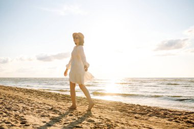 Altın gün batımında sahilde yürüyen genç bir kadın - yaz tatilinde olan kadın turist.