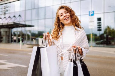 Şehir caddesinde alışveriş torbalarıyla dolaşan güzel genç bir kadın. Satış, alışverişler, alışveriş, yaşam tarzı konsepti.