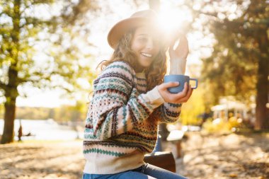 Gülümseyen genç kadın ormanda oturur, çay içer. Seyahatin, tatilin ve sıcak kahvenin tadını çıkar. Yürüyüş yaşam tarzı, macera ve turizm, dinlenme, rahatlama.