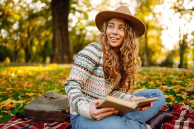 Parkta kitap okuyan bir kadın. Doğanın tadını çıkarma kavramı. Sonbahar havası.