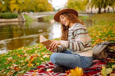 Parkta kitap okuyan bir kadın. Doğanın tadını çıkarma kavramı. Sonbahar havası.