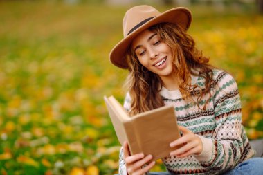 Parkta kitap okuyan bir kadın. Doğanın tadını çıkarma kavramı. Sonbahar havası.